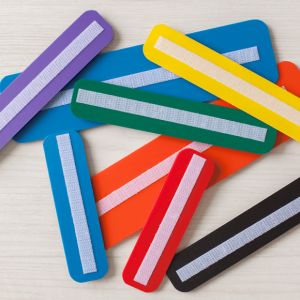 Ensemble de bandes colorées, appellées bandes texte, comportant une bande réfléchissante, posées sur une surface claire.