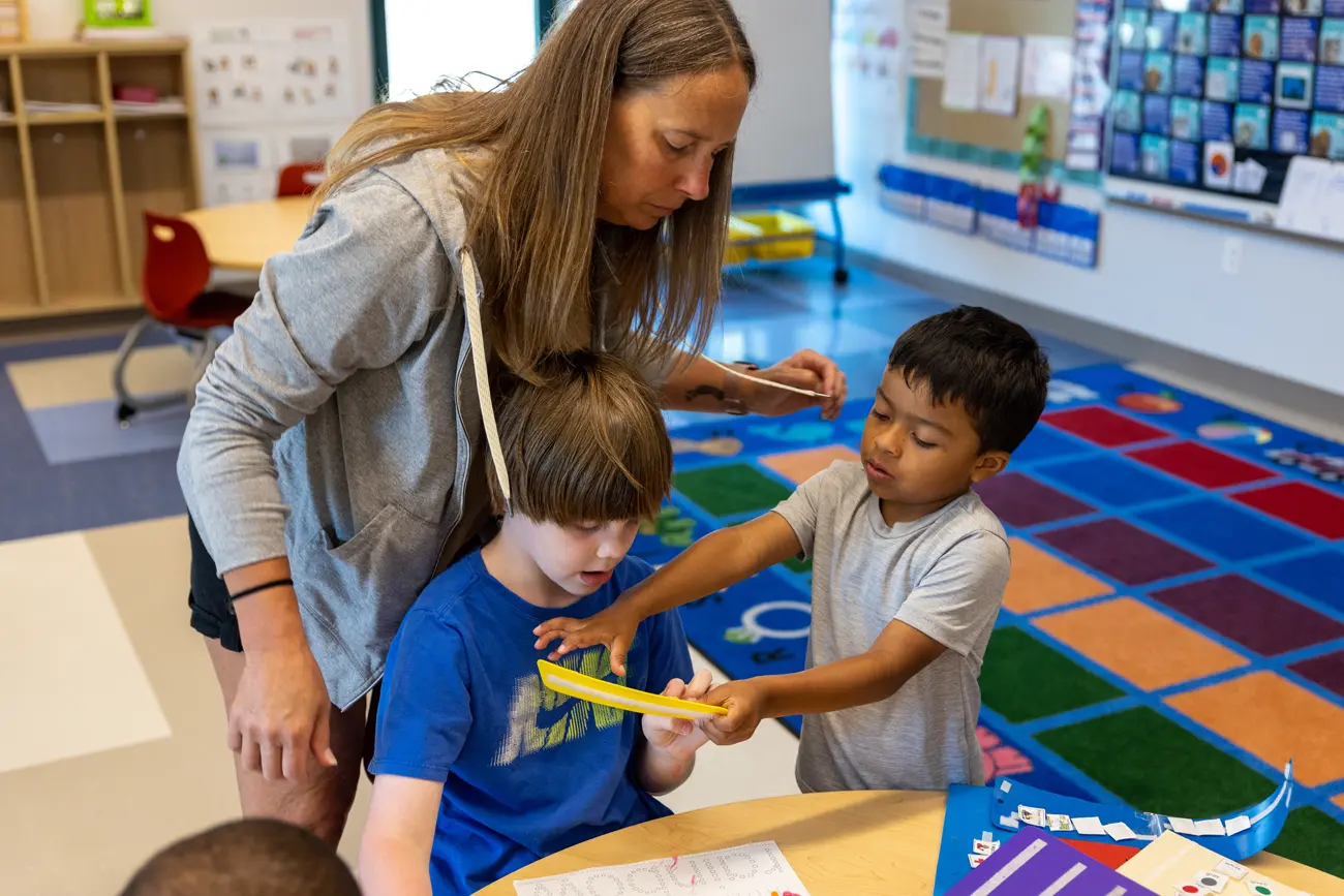 Analyzing-and-Fine-Tuning-Communication Une adulte accompagne deux enfants manipulant une réglette à une table de classe.